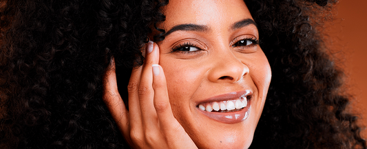 Mulher sorrindo com a mão no rosto. Conheça o poder do retinol. 